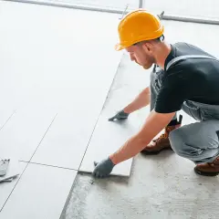 Fachowiec w żółtym kasku układa płytki. Sprawdź, jaka jest układanie płytek cena.