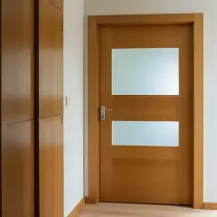 Drewniane drzwi z dwoma przeszkleniami, gotowe do malowania. Obok szafa wnękowa.