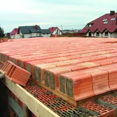 Strop ackermana w budowie, rzędy pustaków ceramicznych czekają na zalanie betonem. W tle domy z czerwonymi dachami.