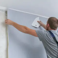 Mężczyzna przykleja tapetę. Zastanawiasz się nad tapetowanie cena? Sprawdź, jak łatwo odmienić wnętrze.