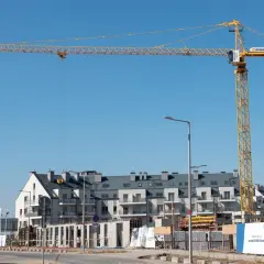 Żółty dźwigar budowlany dominuje nad placem budowy z nowoczesnymi budynkami mieszkalnymi w tle.