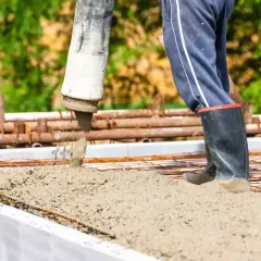 Beton c25/30 wylewany z pompy na zbrojenie. Pracownik w gumowcach stoi w świeżym betonie.