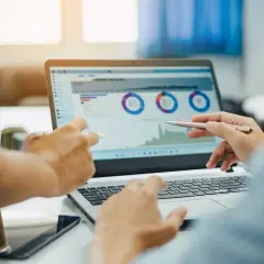 Dwóch ludzi analizuje wykresy na laptopie, dyskutując o prognozach i potencjalnej wartości rezydualnej.
