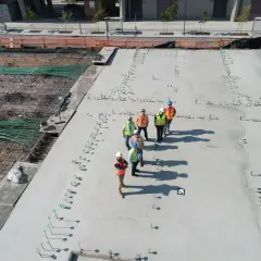 Grupa budowlańców na placu budowy. Widać zbrojenie i świeży beton. Sprawdzają beton b25 cena za m3.