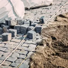 Kostka brukowa i piasek na budowie. Widać stosy kostki i przygotowany pod nią piasek, co sugeruje, ile podsypki pod kostkę na m2 jest potrzebne.