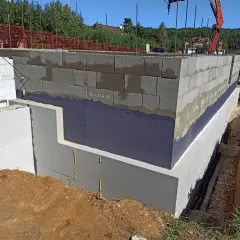 Izolacja fundamentów w starym domu w trakcie budowy. Ściany z bloczków betonowych, izolacja przeciwwilgociowa i termiczna.