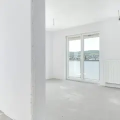 Puste pomieszczenie w stanie deweloperskim, gotowe na wykończenie. Widok na zielone wzgórza z okna. Idealne dla inwestycji na rynku pierwotnym.