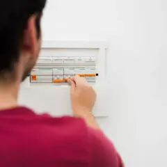 Mężczyzna manipuluje wyłącznikami w skrzynce elektrycznej, co może być pierwszym krokiem, by dowiedzieć się, jak obliczyć zużycie prądu.
