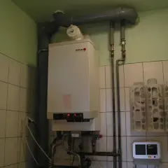 Kocioł gazowy gotowy na sezon grzewczy. W pomieszczeniu z kafelkami widać też termostat i uchwyty na papier toaletowy.