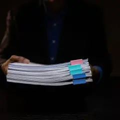 Osoba w garniturze trzyma stos dokumentów z kolorowymi spinaczami, wśród których znajduje się wniosek o wykreślenie hipoteki.