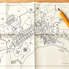 Mapa zasadnicza działki z zaznaczonymi budynkami, drogami i nazwami terenów. Obok leży żółty ołówek.