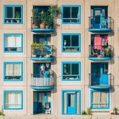 Elegancka loggia i balkon z niebieskimi ramami okiennymi, pełne zieleni i suszącego się prania, tworzą kolorowy wzór na fasadzie budynku.