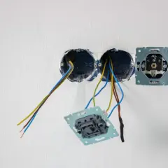Osadzanie puszek elektrycznych w ścianie. Widać przewody wychodzące z dwóch puszek, a obok zamontowaną ramkę gniazdka.