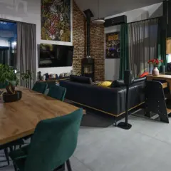 Nowoczesny salon z jadalnią i aneksem kuchennym. Duże okna, ceglana ściana, czarna skórzana kanapa. Zastanawiasz się, jaki koszt budowy domu 120 m?