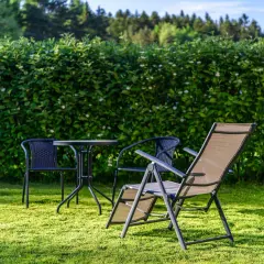 Zielony żywopłot tworzy naturalną barierę, idealną, by odgrodzić się od sąsiada tanio. Stolik i krzesła zapraszają do relaksu.