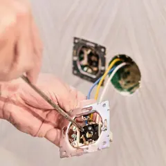 Ręce majsterkowicza montują łącznik dwubiegunowy, przykręcając go śrubokrętem do ściany.