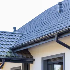 Szary dach z dachówki ceramicznej, rynny i komin. Sprawdź, jaka jest dachówka ceramiczna cena za m2 dla Twojego domu.
