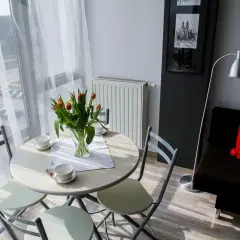 Stół z tulipanami i filiżankami, obok kanapa z czerwoną poduszką. Idealne miejsce na poranną kawę w **garsonierze co to** za urok!