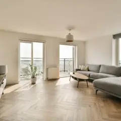 Nowoczesny salon z szarym narożnikiem i drewnianą podłogą. Idealne miejsce do relaksu, gdy rozważasz ceny mieszkań w Lublinie.