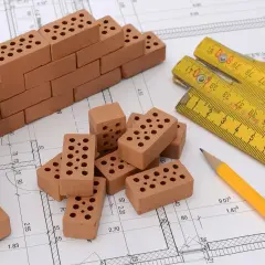 Miniaturowa budowa z cegieł, miarka i ołówek na planie architektonicznym. To idealny zestaw do tworzenia **renta planistyczna**.