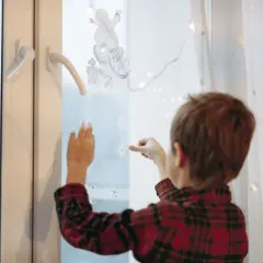 Chłopiec zdejmuje naklejki ze śnieżynkami z szyby, przygotowując się do świąt.
