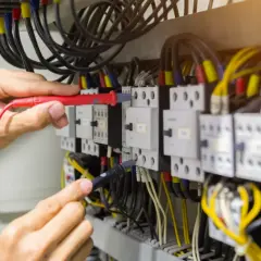 Elektryk sprawdza przewody w szafie sterowniczej. Widać multimetr i liczne kable, w tym przewód neutralny.