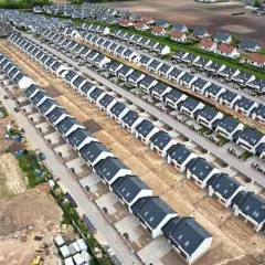 Nowe osiedle domów jednorodzinnych, przykład suburbanizacji. Domy szeregowe z ciemnymi dachami i białymi elewacjami, otoczone placem budowy.