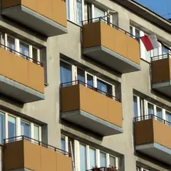 Szukasz informacji, jak dostać mieszkanie komunalne w Łodzi? Zobacz fasadę bloku z żółtymi balkonami i polską flagą.