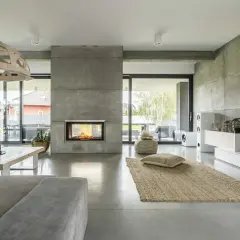 Nowoczesny salon z kominkiem i podłogą z betonu architektonicznego. To właśnie mikrocement nadaje wnętrzu surowego, ale eleganckiego charakteru.