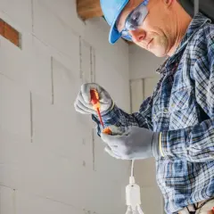 Elektryk w kasku i okularach montuje oprawkę żarówki. Zastanawiasz się, ile za punkt elektryczny?
