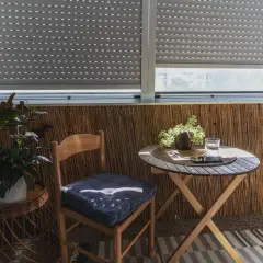 Przytulny balkon typu loggia z drewnianym krzesłem, stolikiem i roślinami. Idealne miejsce na poranną kawę.