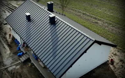 Nowy dach z blachy Budmat. Cennik dostępny online. Dom w trakcie budowy, otoczony zielenią.