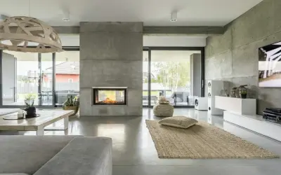Nowoczesny salon z kominkiem i podłogą z betonu architektonicznego. To właśnie mikrocement nadaje wnętrzu surowego, ale eleganckiego charakteru.