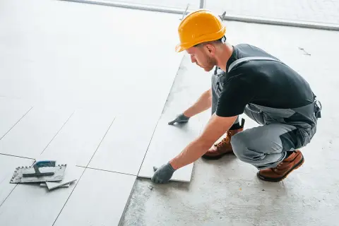 Fachowiec w żółtym kasku układa płytki. Sprawdź, jaka jest układanie płytek cena.