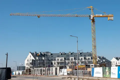 Żółty dźwigar budowlany dominuje nad placem budowy z nowoczesnymi budynkami mieszkalnymi w tle.