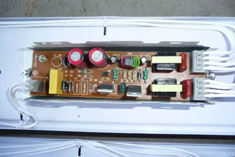 Elektroniczny statecznik z kondensatorami, cewkami i innymi elementami na płytce drukowanej, podłączony białymi przewodami.