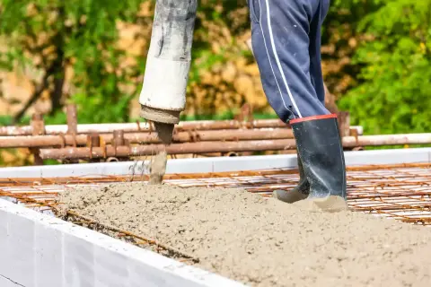 Beton c25/30 wylewany z pompy na zbrojenie. Pracownik w gumowcach stoi w świeżym betonie.