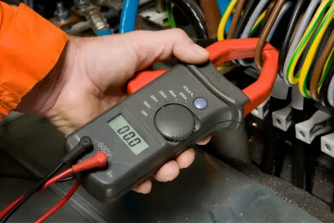 Elektryk mierzy prąd, sprawdzając potencjalny spadek napięcia w instalacji.