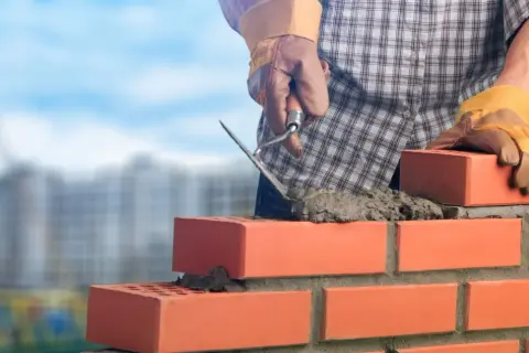 Murarz układa cegły, używając kielni do rozprowadzania zaprawy. Kluczowe są właściwe zaprawa murarska proporcje dla trwałej budowy.