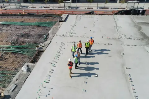 Grupa budowlańców na placu budowy. Widać zbrojenie i świeży beton. Sprawdzają beton b25 cena za m3.