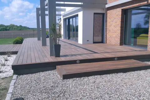 Nowoczesny taras wentylowany, choć piękny, może mieć wady. Widoczna przestrzeń wokół domu z drewnianym tarasem i elementami architektonicznymi.
