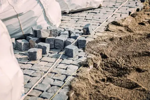 Kostka brukowa i piasek na budowie. Widać stosy kostki i przygotowany pod nią piasek, co sugeruje, ile podsypki pod kostkę na m2 jest potrzebne.