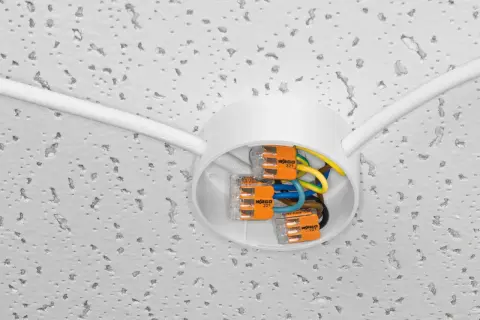 Nowe złącza WAGO ułatwiają wymianę instalacji elektrycznej. Biała puszka sufitowa z kolorowymi przewodami i pomarańczowymi zaciskami.