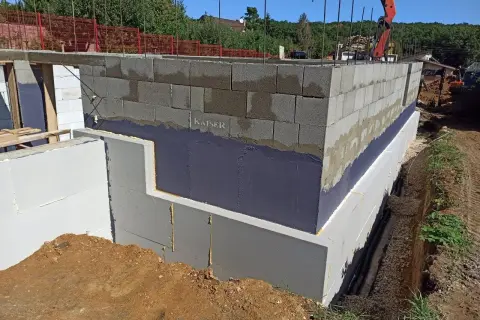 Izolacja fundamentów w starym domu w trakcie budowy. Ściany z bloczków betonowych, izolacja przeciwwilgociowa i termiczna.