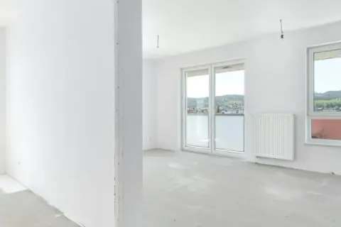 Puste pomieszczenie w stanie deweloperskim, gotowe na wykończenie. Widok na zielone wzgórza z okna. Idealne dla inwestycji na rynku pierwotnym.