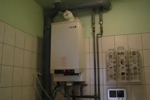 Kocioł gazowy gotowy na sezon grzewczy. W pomieszczeniu z kafelkami widać też termostat i uchwyty na papier toaletowy.