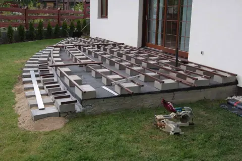 Budowa tarasu kompozytowego: widać betonowe bloczki i legary, co ile legary pod taras kompozytowy.