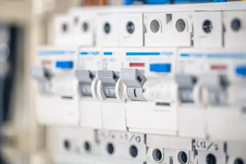 Szukasz informacji, jaki bezpiecznik do gniazdek? Na zdjęciu widać rząd białych wyłączników nadprądowych, każdy z dźwignią i oznaczeniem prądowym.