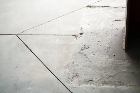 Widoczne pęknięcia i nierówności na posadzce betonowej, wskazujące na potrzebę wykonania dylatacji.