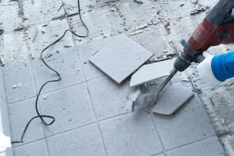Młot udarowy kruszy stare płytki na płytki. Widać kurz i resztki materiału.
